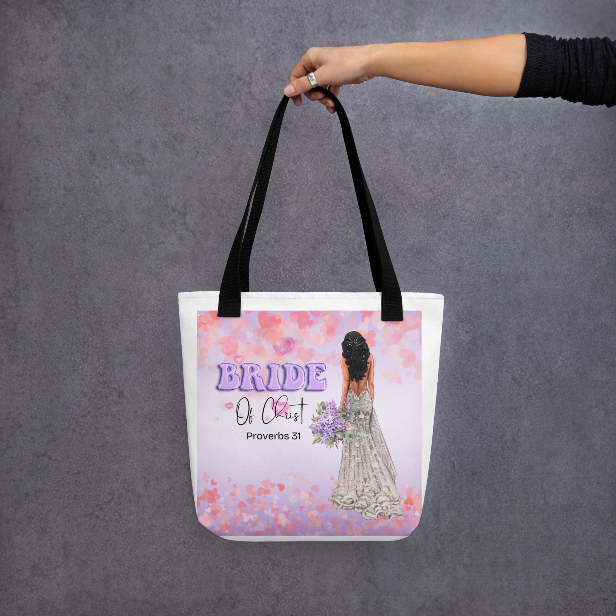 Black handle beige 15x15 canvas tote bag, with square image showing hearts in purple in pink shades, and Balloon text "Bride" in purple with "of Christ" in fancy text with "Proverbs 31" underneath and to the right is back side of Bride, medium skin tone, long dark hair, holding a purple bouquet.
