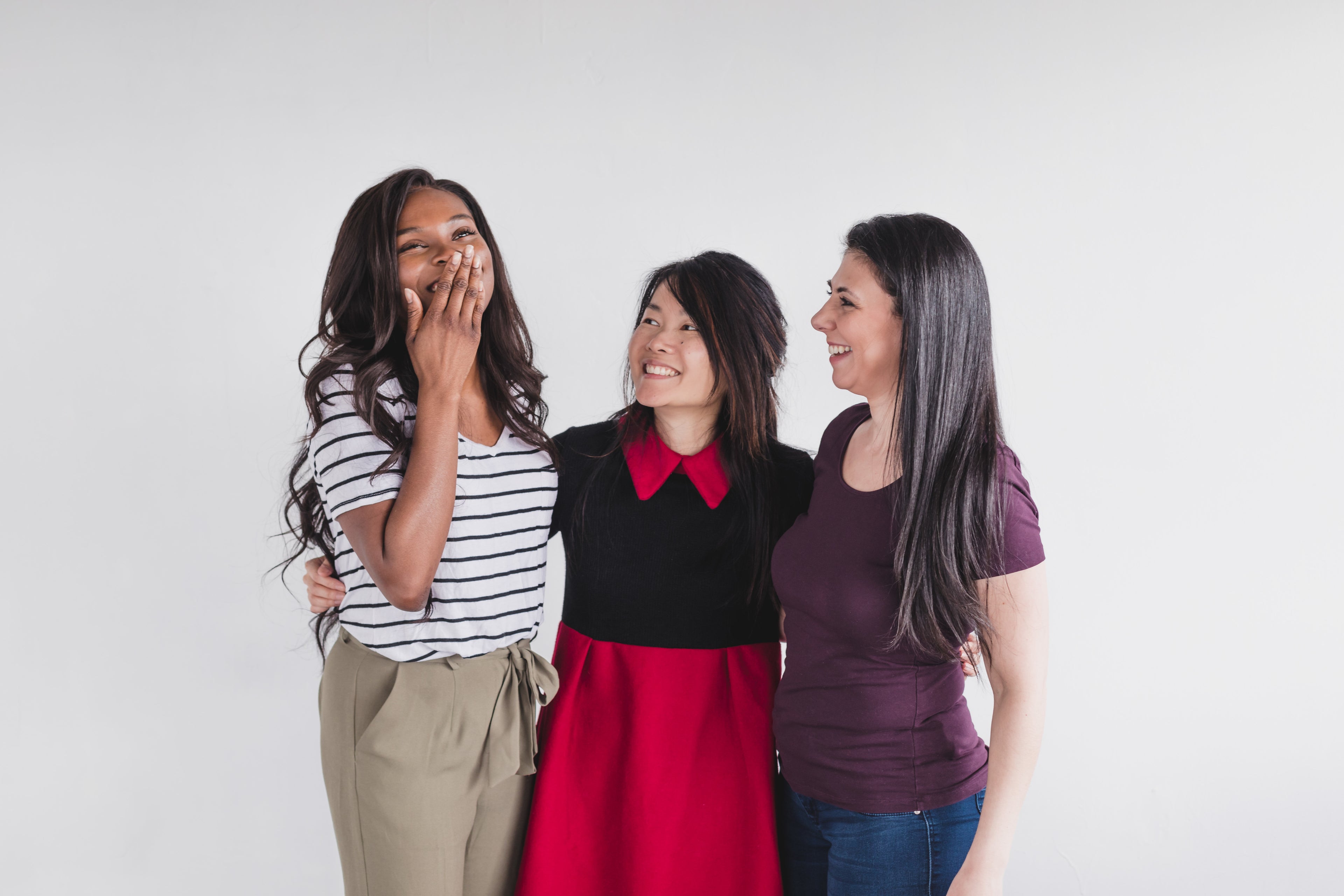 Image of women of different heritage laughing together with a white background
